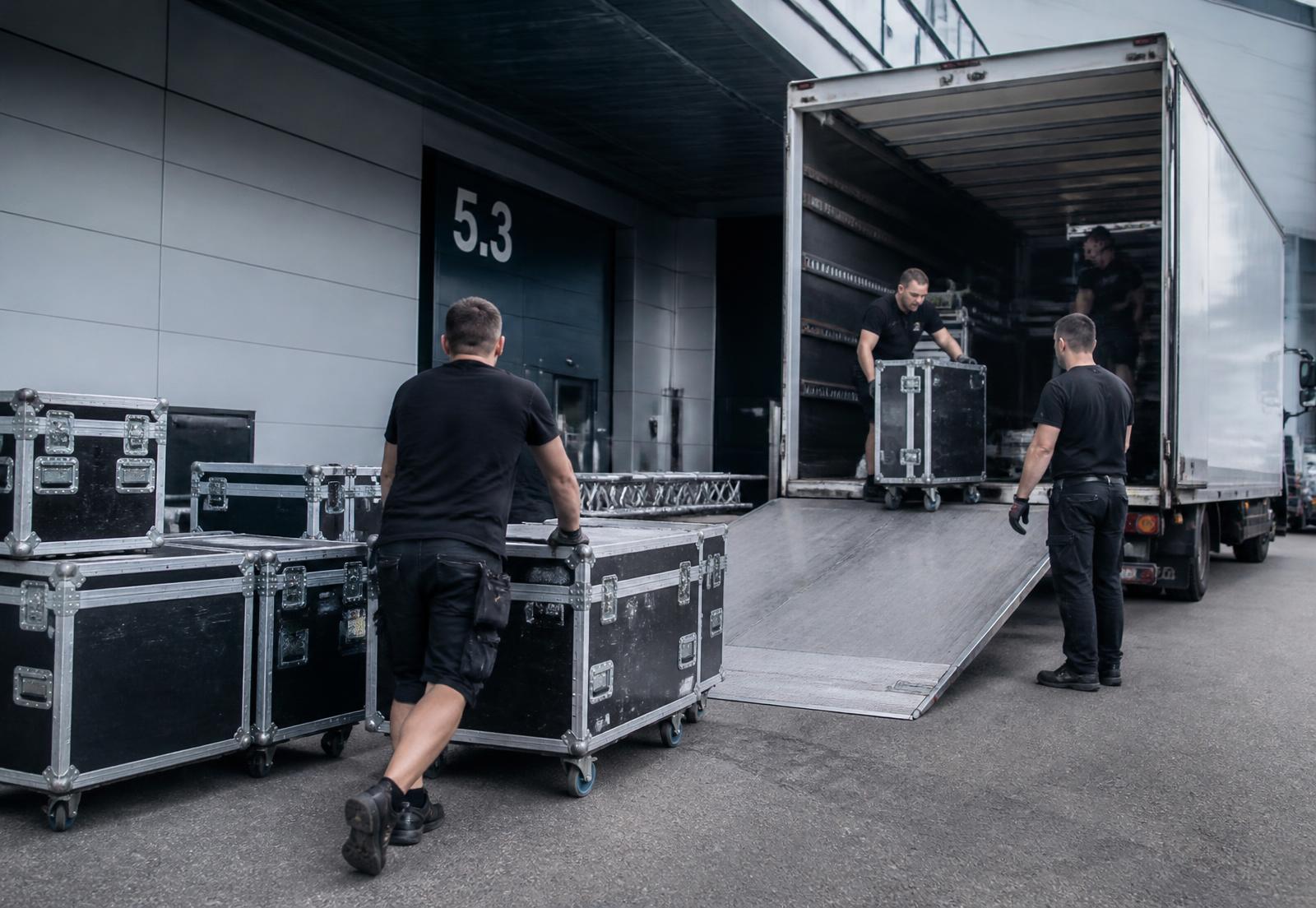 Crew lastar flightcases vid lastkajen till en mässhall